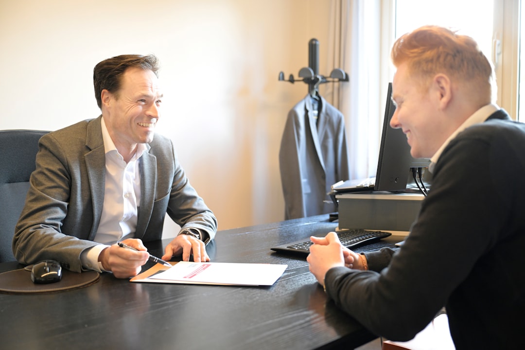 Two smiling men discussing documents at an office desk.